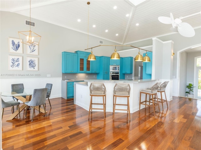 kitchen featuring blue cabinetry, a kitchen bar, appliances with stainless steel finishes, dark hardwood / wood-style floors, and kitchen peninsula