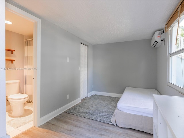 bedroom featuring ensuite bathroom, an AC wall unit, a textured ceiling, and light wood-type flooring