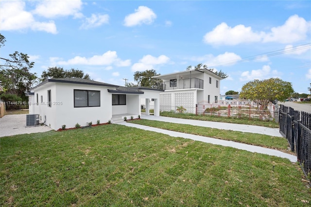 view of front of property with fence private yard, a balcony, central AC, stucco siding, and a front lawn