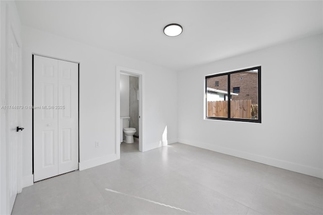 unfurnished bedroom featuring ensuite bathroom, a closet, and baseboards