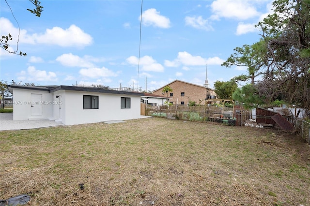 rear view of house featuring a lawn, fence, and stucco siding