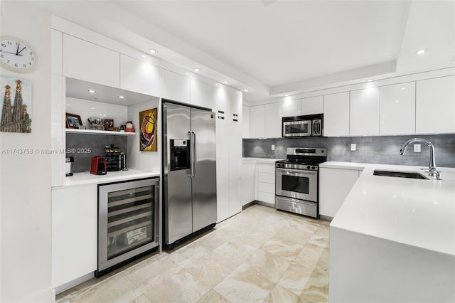 kitchen with sink, appliances with stainless steel finishes, white cabinetry, wine cooler, and tasteful backsplash