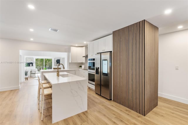 kitchen with white cabinetry, sink, a breakfast bar area, light hardwood / wood-style floors, and stainless steel appliances