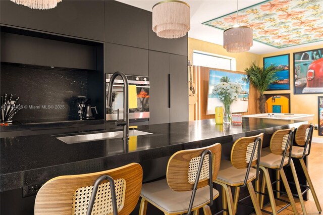 kitchen with decorative light fixtures, oven, sink, and a breakfast bar area