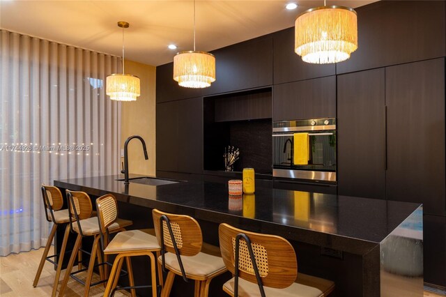 bar featuring sink, light wood-type flooring, oven, hanging light fixtures, and an inviting chandelier