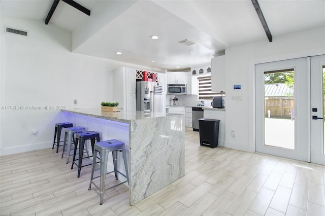 kitchen with a breakfast bar area, stainless steel appliances, light stone countertops, white cabinets, and kitchen peninsula