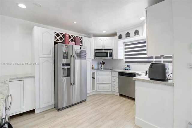 kitchen with white cabinetry, appliances with stainless steel finishes, light stone countertops, and light wood-type flooring