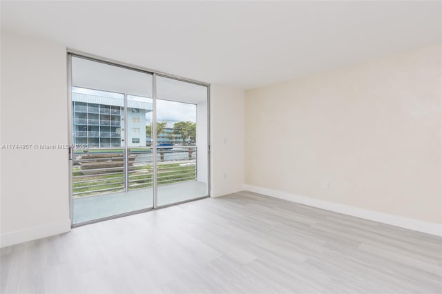 empty room with floor to ceiling windows and light hardwood / wood-style flooring