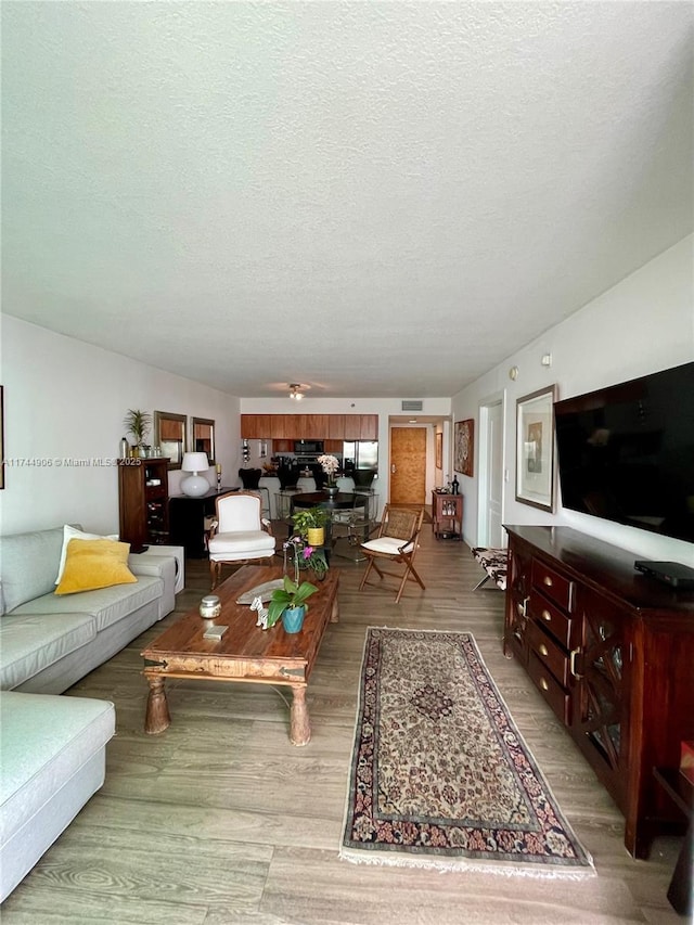 living room featuring ceiling fan, light hardwood / wood-style flooring, and a textured ceiling