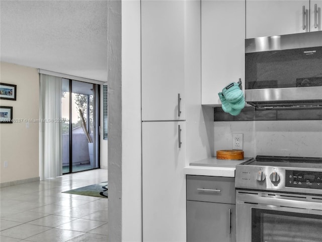 kitchen with a textured ceiling, light tile patterned floors, expansive windows, stainless steel appliances, and white cabinets