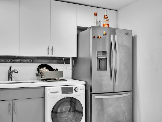 kitchen featuring stainless steel fridge with ice dispenser, washer / dryer, sink, and white cabinets