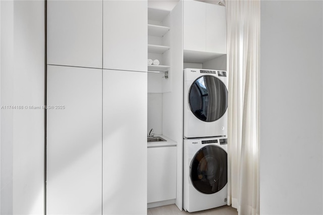 washroom with sink, stacked washer / drying machine, and cabinets