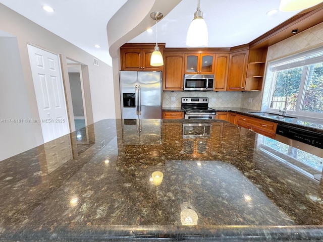 kitchen featuring tasteful backsplash, appliances with stainless steel finishes, dark stone counters, and decorative light fixtures