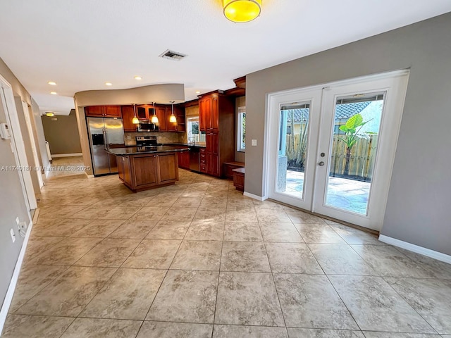 kitchen with french doors, a kitchen island, pendant lighting, stainless steel appliances, and backsplash