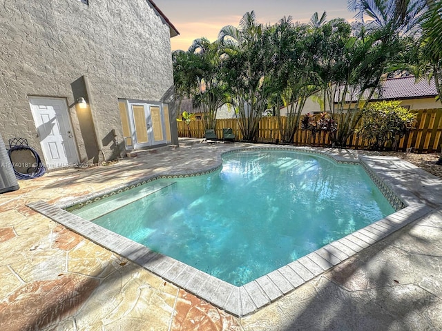 pool at dusk featuring a patio and french doors