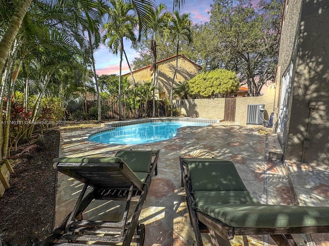 pool at dusk with a patio and central air condition unit