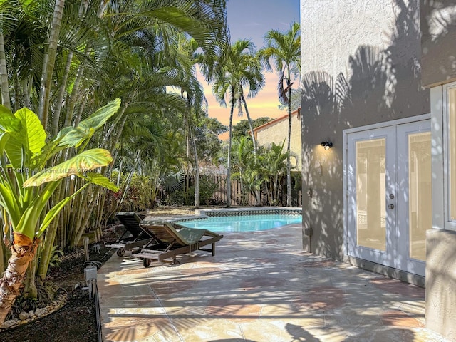 pool at dusk with a patio area and french doors