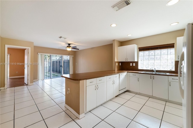 kitchen featuring a peninsula, white appliances, a sink, white cabinetry, and dark countertops