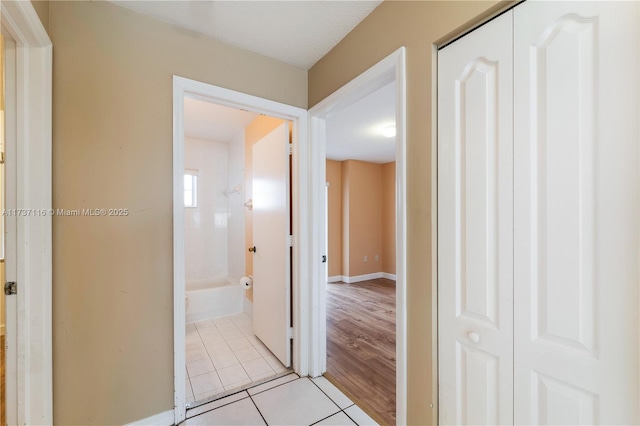 hall featuring light tile patterned flooring and baseboards