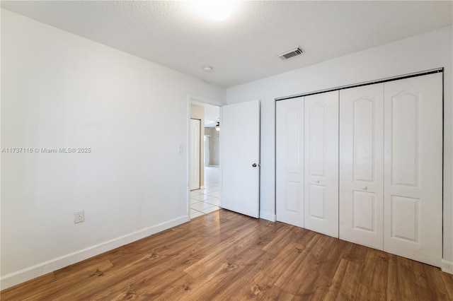 unfurnished bedroom featuring a textured ceiling, light wood-style flooring, visible vents, baseboards, and a closet