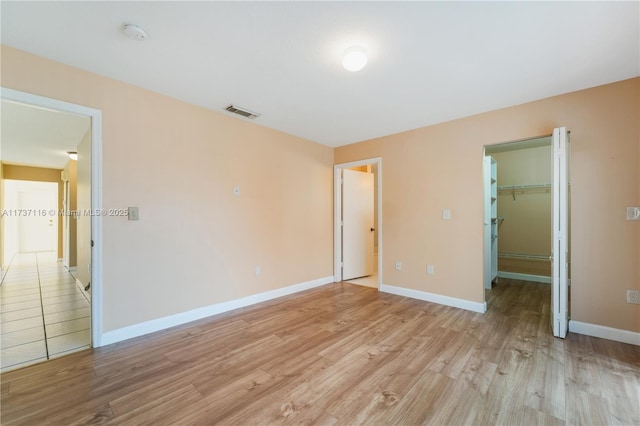 unfurnished bedroom with light wood finished floors, a closet, visible vents, a spacious closet, and baseboards