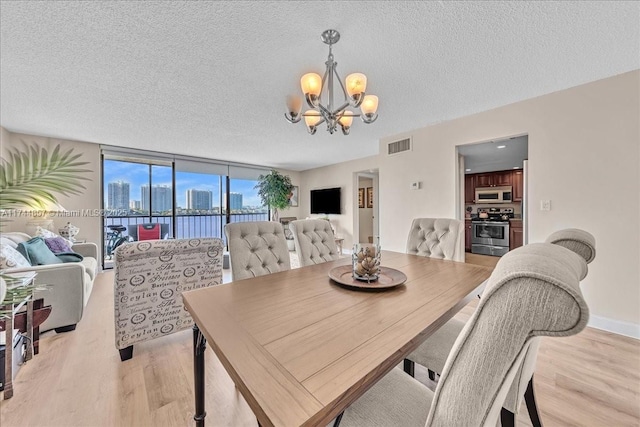 dining area featuring a chandelier, a textured ceiling, light wood-type flooring, and a wall of windows