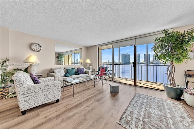 living room with a water view, expansive windows, light hardwood / wood-style floors, and a textured ceiling