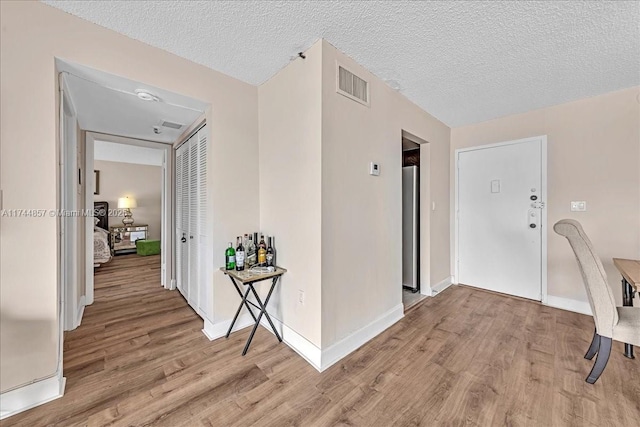 hall with light hardwood / wood-style floors and a textured ceiling