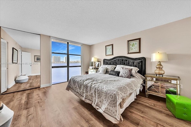 bedroom featuring expansive windows, a water view, hardwood / wood-style floors, and a textured ceiling