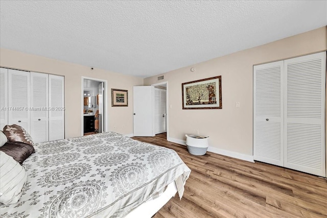 bedroom featuring multiple closets, ensuite bath, hardwood / wood-style floors, and a textured ceiling