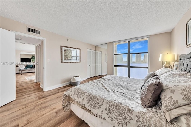 bedroom with a water view, a textured ceiling, a closet, a wall of windows, and light hardwood / wood-style floors