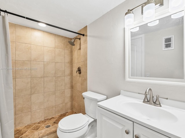 bathroom featuring visible vents, toilet, tiled shower, and vanity