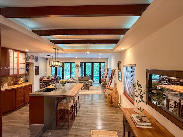 kitchen featuring an island with sink, glass insert cabinets, a kitchen breakfast bar, wood finished floors, and light countertops