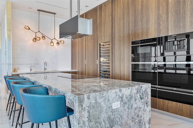 kitchen featuring a breakfast bar area, a spacious island, light stone counters, black electric stovetop, and decorative light fixtures