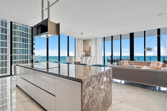 kitchen with a water view, dark stone countertops, a kitchen island, a wall of windows, and white cabinets