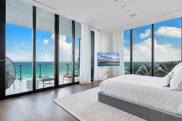 bedroom featuring floor to ceiling windows, a water view, wood-type flooring, and access to outside