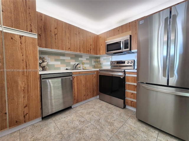 kitchen with light tile patterned floors, a sink, light countertops, brown cabinets, and stainless steel appliances