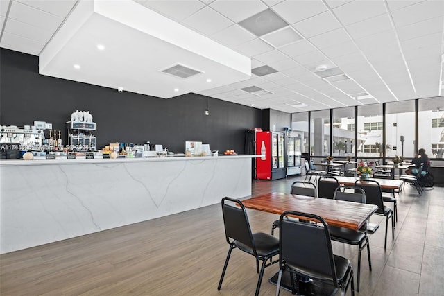 dining area featuring a drop ceiling, a wall of windows, and wood-type flooring