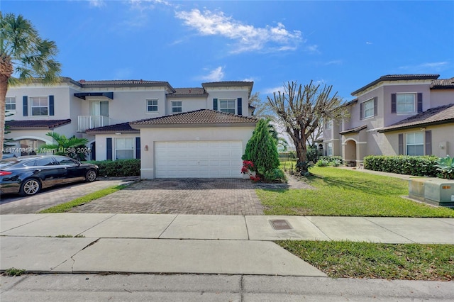 view of property featuring stucco siding, driveway, a tile roof, a front yard, and an attached garage