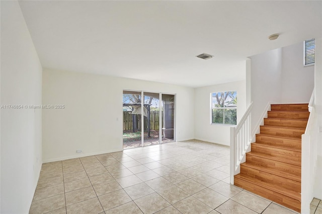 unfurnished room featuring light tile patterned flooring, visible vents, stairs, and baseboards