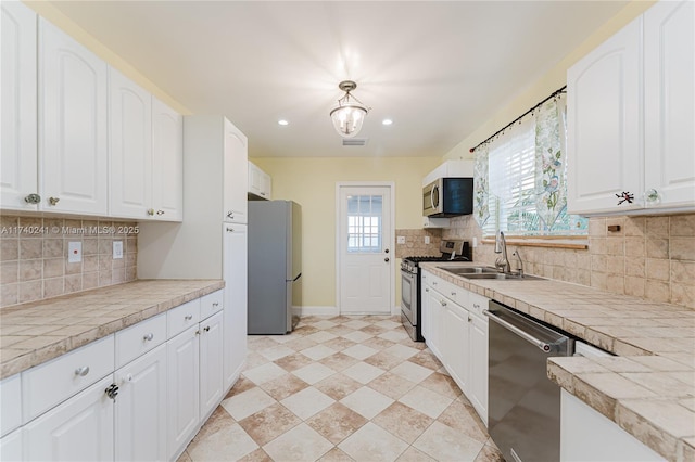 kitchen with tasteful backsplash, hanging light fixtures, stainless steel appliances, white cabinets, and sink