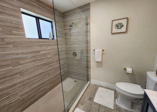 bathroom with tiled shower, wood-type flooring, toilet, and vanity