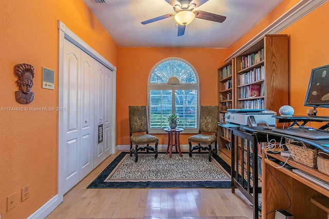 sitting room with a textured ceiling, hardwood / wood-style flooring, baseboards, and ceiling fan