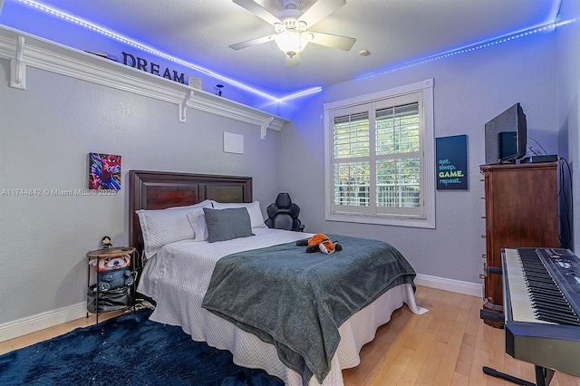 bedroom with a textured wall, a ceiling fan, baseboards, and wood finished floors