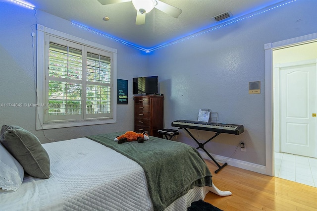 bedroom with ceiling fan, wood finished floors, visible vents, and baseboards