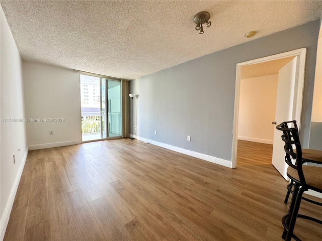 unfurnished room featuring expansive windows, a textured ceiling, baseboards, and wood finished floors