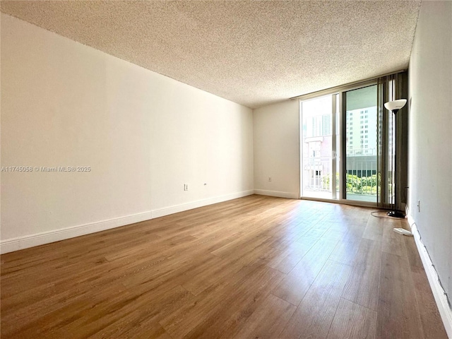 empty room featuring expansive windows, a textured ceiling, wood finished floors, and baseboards