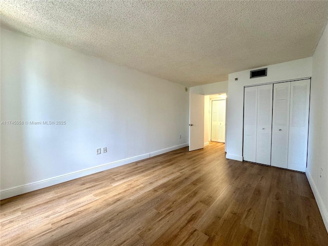 unfurnished bedroom with visible vents, baseboards, wood finished floors, a textured ceiling, and a closet