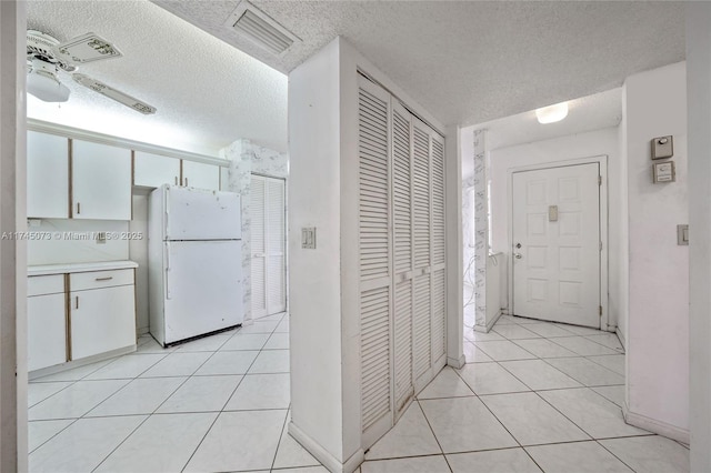 kitchen featuring light countertops, freestanding refrigerator, white cabinets, and light tile patterned floors