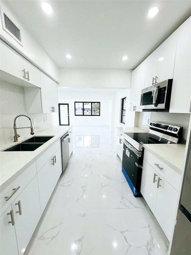 kitchen featuring appliances with stainless steel finishes, light countertops, a sink, and white cabinetry